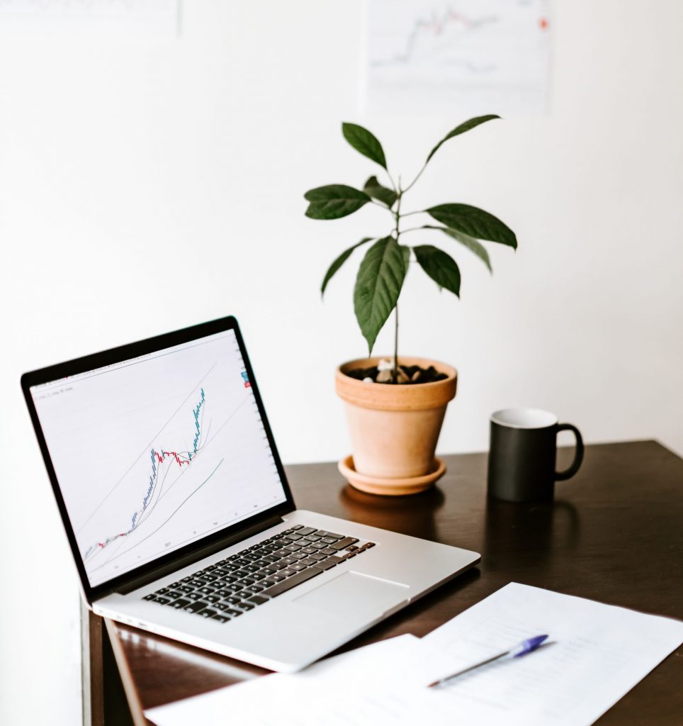 workplace of investment manager with with green plant and cup of coffee. stocks price rising graph data trend laptop screen.